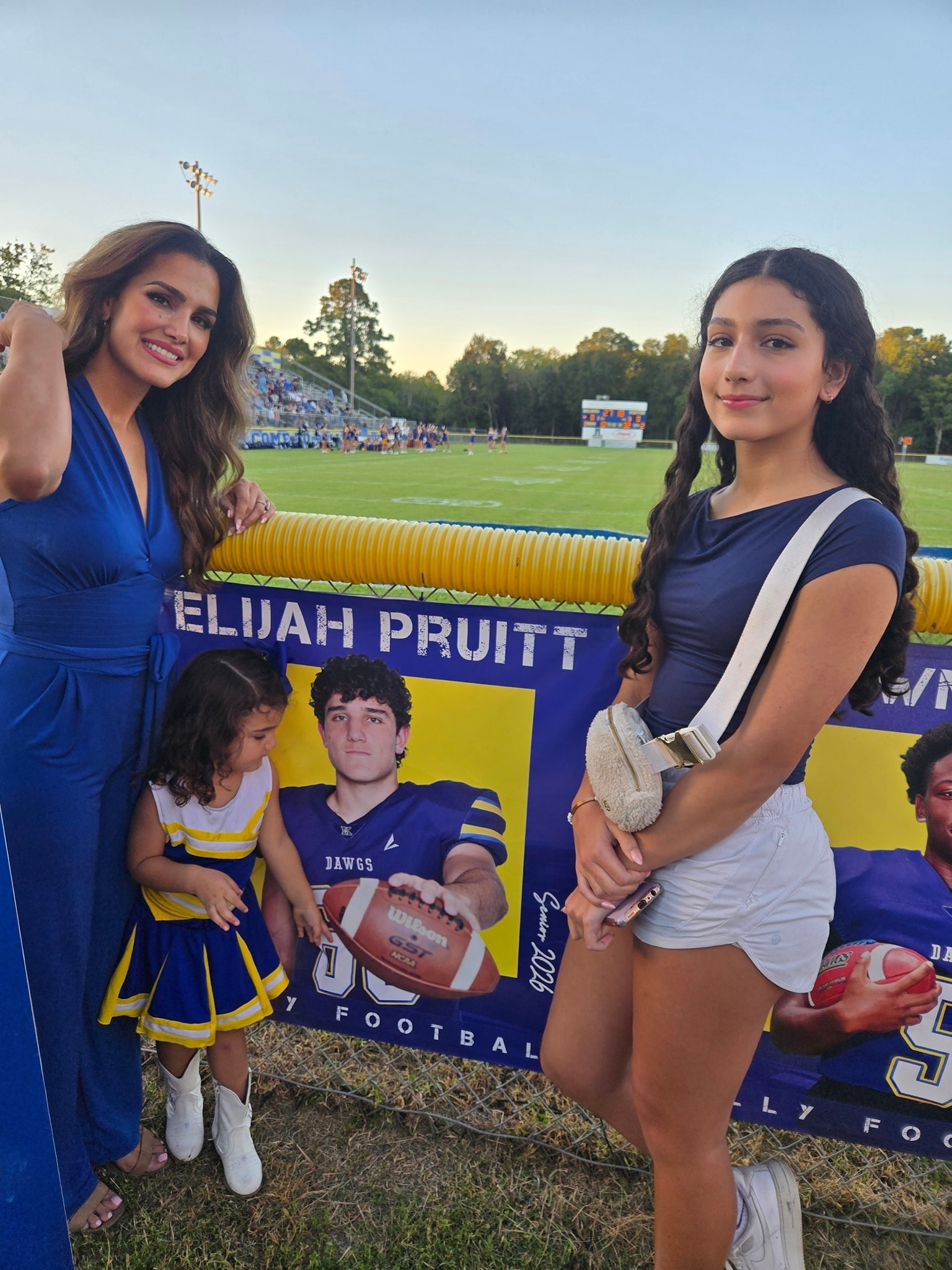 Priscilla, Elle, and Adonai in front of Elijah's football poster